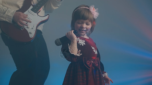 穿旧礼服的小女孩在舞台上唱歌 她父亲弹电吉他裙子长袍婴儿衣服爸爸蕾丝彩色油烟机连衣裙蓝色图片