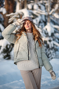 一个模范女孩在雪覆盖的森林中行走 展示着衣服乐趣女性松林季节毛衣帽子外观外套幸福微笑图片