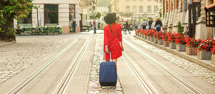 美丽的年轻女孩带着蓝色手提箱走来走去风景行人女士帽子电车晴天游客行李街道建筑图片