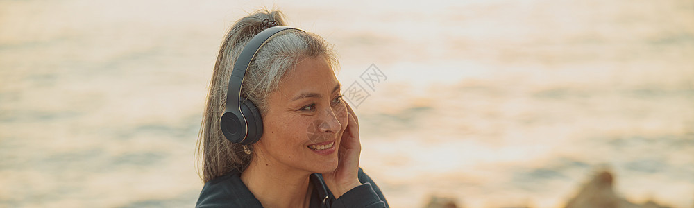 用耳机坐在海边的亚洲女士图片