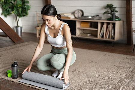 亚洲健身女孩完成训练 在家打运动 在客厅锻炼后滚动地板垫 清洁等笔记本运动员营养成人有氧运动冥想活力互联网瑜伽电脑图片