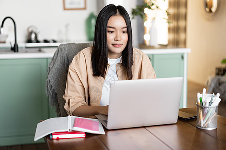 在家学习的亚洲女孩 远程教育理念 女学生用笔记本电脑学习 远程工作的年轻女性 坐在厨房里 拿着书和电脑课程互联网口罩乐趣休息微笑图片