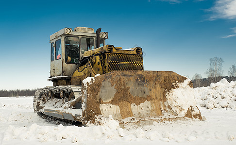 带桶的黄色履带式拖拉机推土机在冬天清理道路积雪 寒冷的一天 明亮的阳光和美丽的蓝天在背景中 黄色推土机在冬天打扫运输力量风暴活动图片