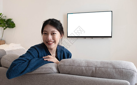 在一个快乐的亚洲女人面前看着镜头 在沙发上的白色电视后面 在家里客厅里 (笑声)图片