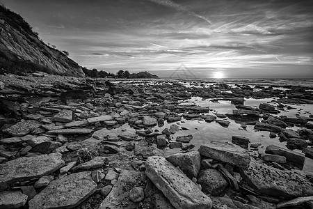 令人惊异的日出在海面上 岩石般的海岸是黑白的图片