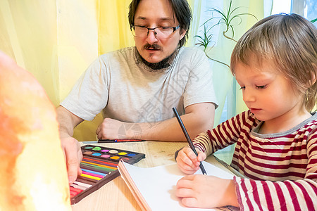 穿着灰色T恤的胡子男子和可爱男孩在家中共度时光时 用彩蜡笔绘画创造力婴儿桌子父母家庭儿童成人艺术男性微笑图片