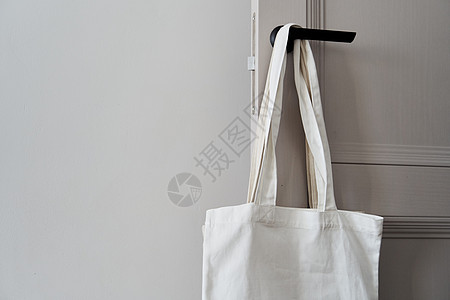 白色生态友好袋挂在门把手上 罐装袋织物嘲笑模板礼物市场背景手工购物木材帆布包图片