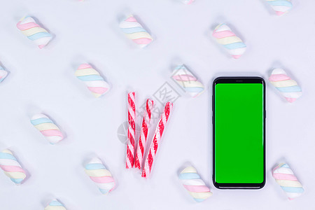 有一个垂直的绿色屏幕的电话移动电话 拐杖糖圣诞糖果 带有扭曲的棉花糖图案的白色背景 色键智能手机技术 电话样机图片
