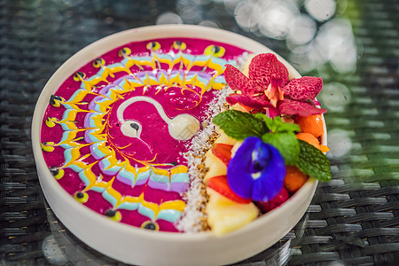 健康的热带早餐 带热带水果的冰沙碗 装饰着彩色酸奶 姜黄和螺旋藻的图案 它还装饰有水果 鲜花 奇亚籽 椰子 格兰诺拉麦片 菠萝 图片