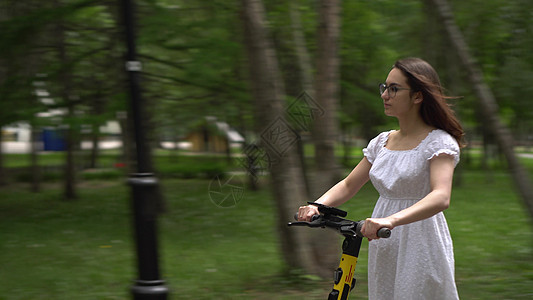身着白裙子的年轻亚洲女人骑着一辆共用电动摩托车在公园里 戴着眼镜的女孩生态城市女性自行车游客女士创新成人运输青菜图片
