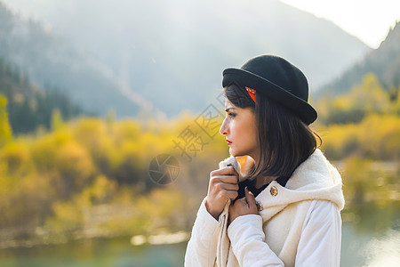 身穿白大衣的年轻女子在自然界中行走 向外望去 从秋天寒冷处躲起来图片