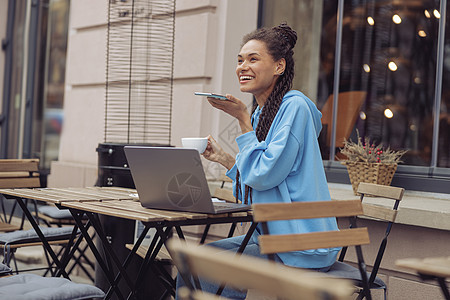 相当开心的年轻女子 用笔记本电脑发送语音信息 在咖啡厅露台喝咖啡图片