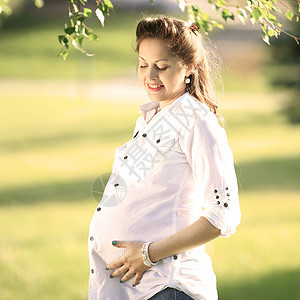 美丽的孕妇 在公园外面放松的美丽女士父母母亲树木成人母性女性生育力阳光怀孕微笑图片