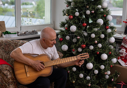 快乐的人的家庭观念  圣诞节时 老人在家里的沙发上享受吉他女士购物爸爸盒子丝带音乐乐趣房间喜悦派对背景图片