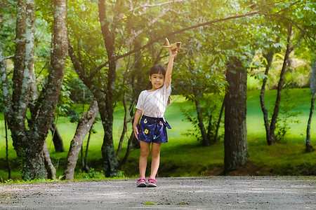 快乐的小女孩在夏日公园里玩纸板做的飞机 可爱的小女孩带着一架玩具飞机在公园的路上奔跑 快乐的童年概念娱乐手工家庭教育乐趣晴天生态图片