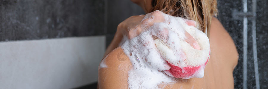 手泡沫女人用海绵和淋浴胶洗身体背景