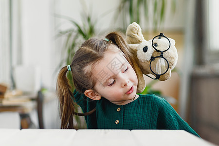 甜美的小女孩正在玩一只戴着圆形眼镜的木偶熊 待在家里时微笑着图片