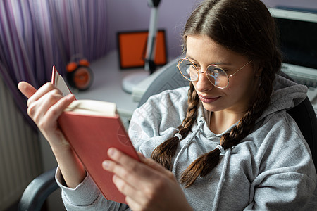一个带着眼镜笑着的青少年在家里读学校的书戴眼镜长发学生青年读书知识窗户谎言爱好者椅子图片