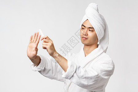 美人 SPA和休闲概念 穿着浴袍和浴巾的英俊亚洲男子肖像 看着手指并微笑快乐 油钉 修指甲 白色背景成人抛光浴衣长袍护理闲暇皮肤图片