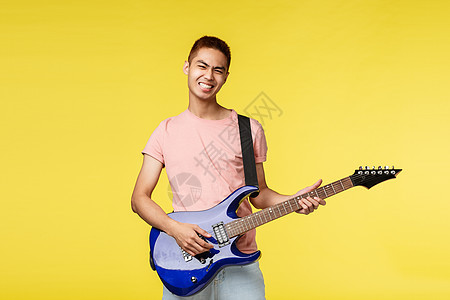 生活方式 休闲和青年概念 让果酱 无忧无虑的微笑亚洲人在乐队里演奏 拿着蓝色电吉他 感觉摇滚乐从舞台上开始 站在乐观的黄色背景中图片