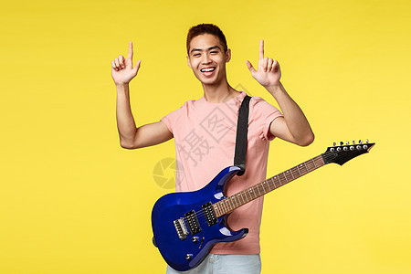 生活风格 休闲和青年概念 充满热情的英俊年轻的亚洲男性举起手指 在舞台上表演 拿着电吉他和笑脸 黄色背景快乐地享受着吉他歌手手势图片
