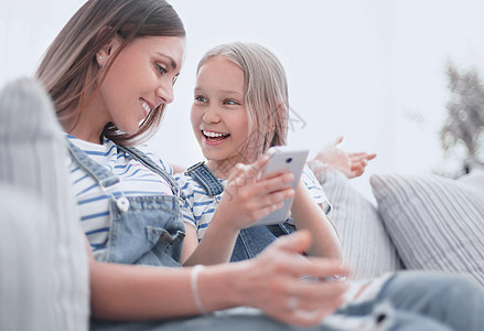 快乐的妈妈和女儿正在观看智能手机视频 笑声女孩照片家庭童年技术孩子微笑沙发幸福女性图片