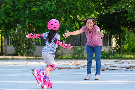 亚裔母亲帮助女儿在公园练习溜冰 为孩子们的户外活动提供启迪溜冰鞋享受学习爱好童年头盔平衡女性家庭快乐图片