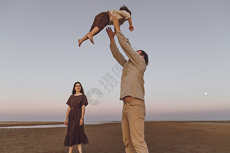 年幼的父母在海边海滩上玩儿孩子 父亲的欢乐将儿子吐在空中图片