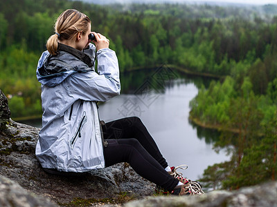 观光女孩在湖边森林的岩石上游荡着一个女孩远足活动光学远足者望远镜绿色游客冒险旅行勘探图片