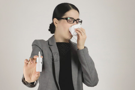 身穿灰色夹克和眼镜的年轻女性过敏 手持过敏鼻腔喷雾图片