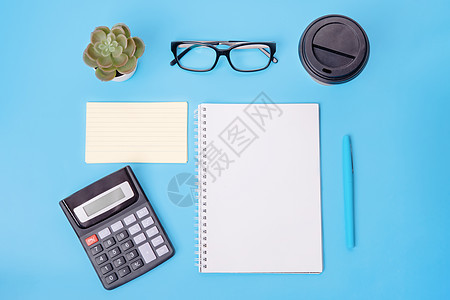 蓝色背景上的计算器 空白 便条纸 纸 咖啡 眼镜 植物和钢笔 工作场所 文本空间 财务支票图片