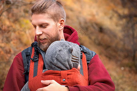 可爱的留着胡须的婴儿父亲和他的儿子在秋季户外婴儿背带中的肖像图片