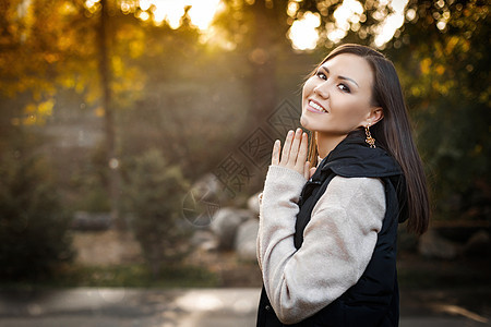 照片右侧微笑的年轻女子秋天站在户外 穿着温暖的毛衣和无袖夹克图片