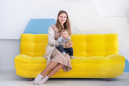 一名欧洲年轻女子的肖像 她带着一个小孩坐在沙发上 内地非常积极童年保姆男生黄色母爱儿子母性金发婴儿家庭图片