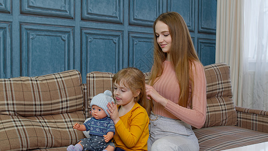 女人照顾 在客厅里梳理妹妹的头发 孩子玩玩具娃娃图片