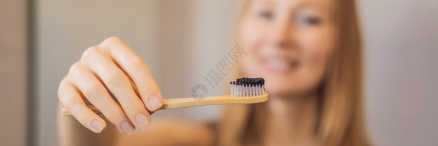 年轻女子用黑牙糊刷牙 在洗手间AANNER(Long ForMAT)使用活性木炭和黑牙刷来刷牙图片
