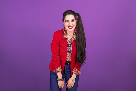 快乐笑笑的年轻黑发女人 在90年代风格 穿红色外套 紫色背景图片