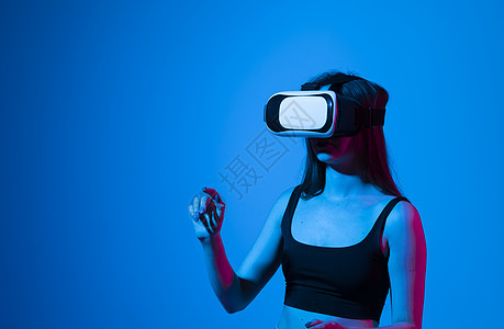 在蓝色背景的霓虹灯下戴着 VR 眼镜玩耍的年轻女子的画像 概念现代小工具和技术 未来的技术概念 虚拟现实游戏高科技模拟器女性视频图片