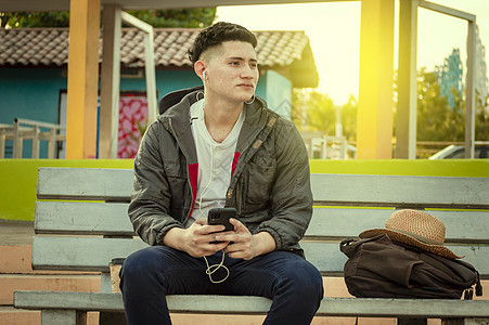 一个在长椅上听音乐的帅哥 一个坐在长椅上用手机听音乐的拉丁男人图片