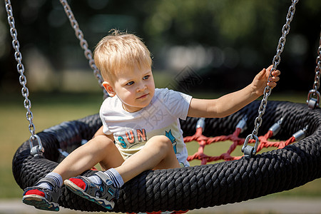 可爱笑脸的小男孩在太阳公园的儿童游乐场上骑着摇摆吊床玩耍 街头活动的概念图片