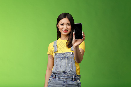 自信自信的漂亮亚洲女性介绍智能手机应用程序 伸出手持电话臂 微笑高兴 推荐社交资料 吹嘘自己的博客 绿色背景工作情绪促销学生旅游图片