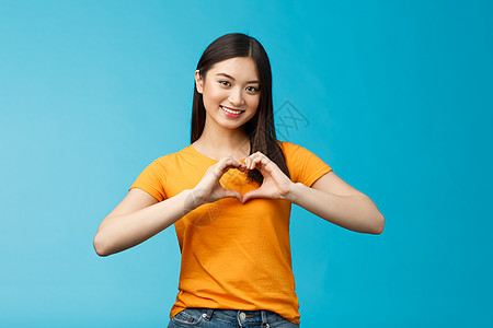 可爱 有爱心 有魅力的亚洲女友表现出珍惜和重视关系的心 微笑着广泛支持 站在蓝色背景上 穿黄色 T 恤 促进和平与幸福皮肤工作室图片