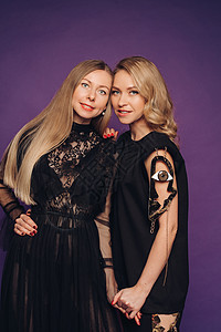 两姐妹在工作室摆紫色背景的姿势 两个穿黑花丽裙的美女 聚在一起参加派对发型黑发双胞胎朋友们头发夫妻幸福乐趣友谊成人图片