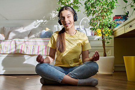 听耳机的少女在家中坐在莲花姿上放松房间头脑青春期播客青年娱乐享受地面歌曲瑜伽图片