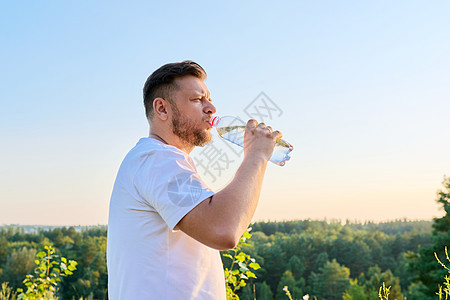 中年男子在阳光明媚的夏日用瓶子喝水图片