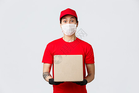 身穿红色制服帽和 T 恤 拿着客户订单的盒子 戴着医用口罩和防护手套 在大流行冠状病毒期间确保安全的惊喜快递员 送货员带来您的订图片