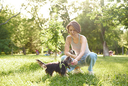 约克夏犬的女主人在草地上玩得很开心 小狗宠物和女人一起跑步 让朋友慢跑 在户外公园搞笑 跑道和锻炼图片