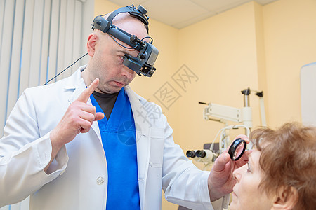 一名男性眼科医生用双目检眼镜检查一名成年女性的视力病人眼睛治疗显微镜诊断测量配镜师咨询药品头盔图片