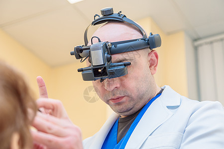 一名男性眼科医生用双目检眼镜检查一名成年女性的视力病人治疗近视头盔眼力考试显微镜乐器办公室折射图片