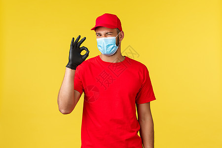 大流行期间的快递 covid-19 安全运输 购物概念 身穿红色制服和医用口罩的快递员 来自冠状病毒的个人防护装备 眨眼并显示好图片